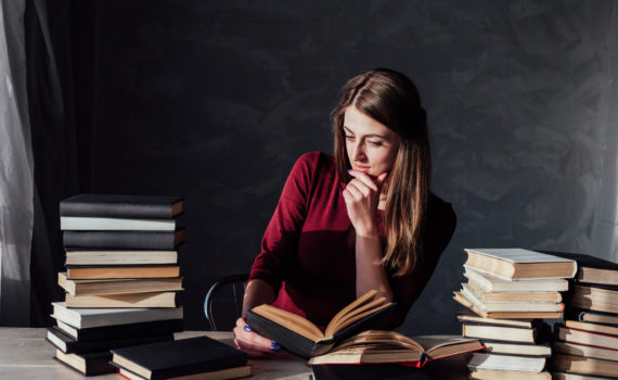 the girl sitting at the table reading a lot of books the girl sitting at the table reading a lot of books library
